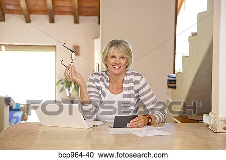 Stock Image - Woman working at home office with computer and bills. Fotosearch