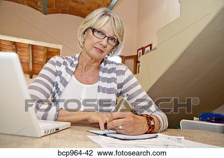 Stock Image - Woman working at home office with computer and bills. Fotosearch