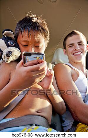 Stock Image - Boys in backseat of car with phone. Fotosearch