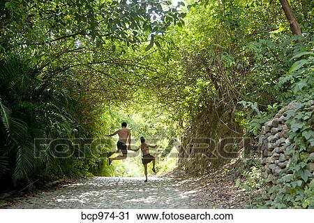 Stock Image - Couple jumping in air on tree arched path. Fotosearch