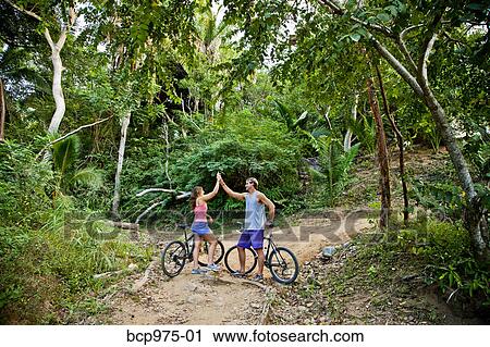 Stock Image - Couple riding bicycles on jungle path. Fotosearch