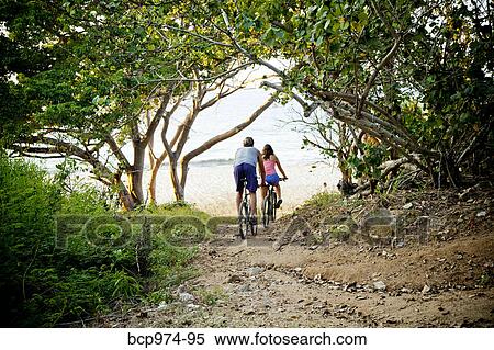 Stock Photography - Couple riding bicycles on path to beach. Fotosearch