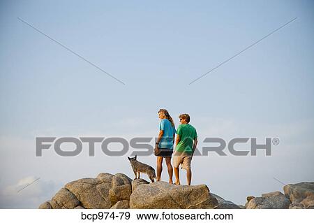 Stock Photo - Couple with dog hiking on beach rocks. Fotosearch