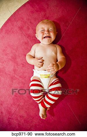 Stock Image - Crying baby on pink rug. Fotosearch