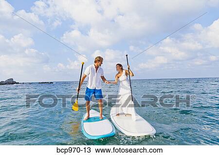 Stock Image - Dressed up mad and woman riding paddle boards. Fotosearch