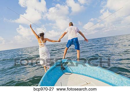 Stock Photo - Dressed up man and woman jumping off boat. Fotosearch