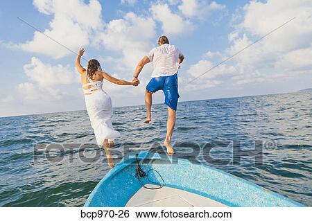 Stock Photograph - Dressed up man and woman jumping off boat. Fotosearch