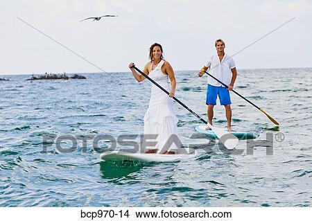Picture - Dressed up man and woman riding paddle boards. Fotosearch
