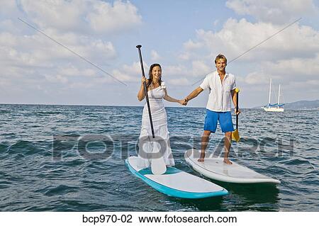 Stock Image - Dressed up man and woman riding paddle boards. Fotosearch