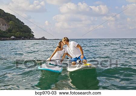 Stock Image - Dressed up man and woman riding paddle boards. Fotosearch