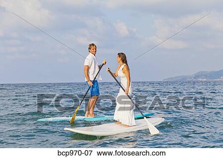 Stock Photo - Dressed up man and woman riding paddle boards. Fotosearch