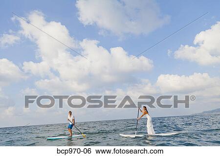 Stock Photograph - Dressed up man and woman riding paddle boards. Fotosearch