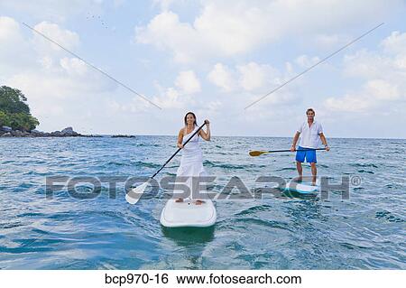 Stock Photograph - Dressed up man and woman riding paddle boards. Fotosearch