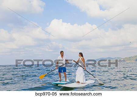 Stock Photography - Dressed up man and woman riding paddle boards. Fotosearch