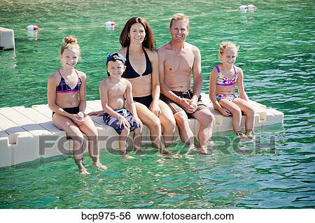 Stock Photograph - Family sitting on dock in lake. Fotosearch