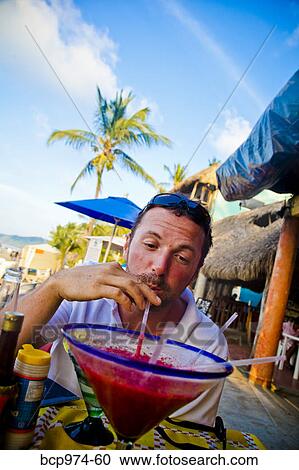 Stock Image - Man drinking oversized cocktail. Fotosearch