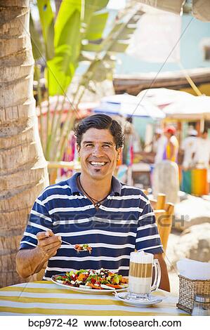 Stock Image - Man eating at outdoor café. Fotosearch