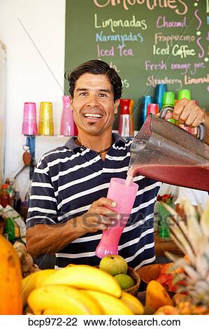 Stock Image - Man pouring smoothie in caf. Fotosearch