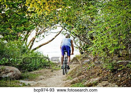 Stock Image - Man riding bicycle on path to beach. Fotosearch