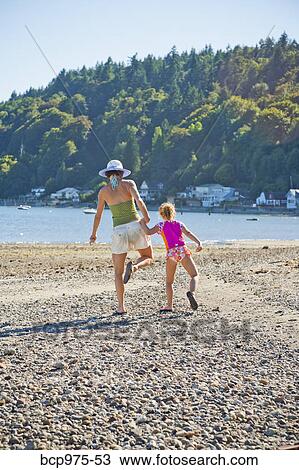 Stock Image - Mother and daughter walking down beach. Fotosearch