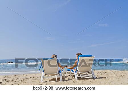 Stock Photo - Rear view of couple in beach chairs. Fotosearch