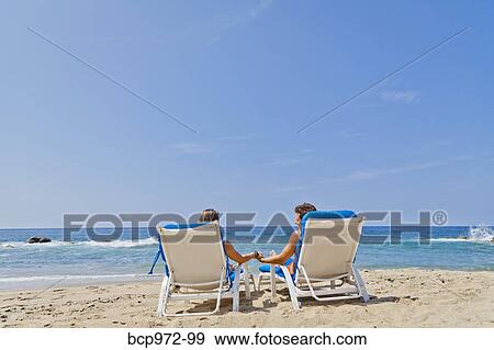Stock Photo - Rear view of couple in beach chairs. Fotosearch