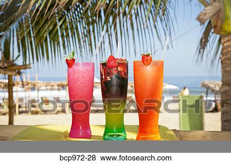 Stock Photo - Row of colorful drinks on seaside table. Fotosearch