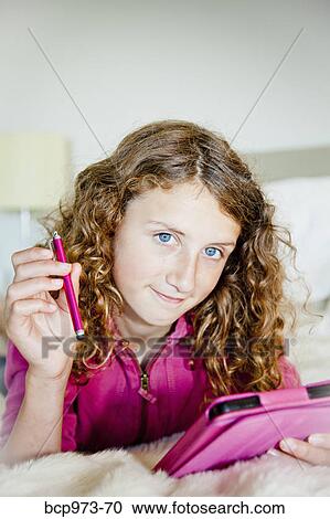 Stock Image - Teen girl on bed with tablet. Fotosearch