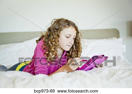 Teen girl on bed with tablet View Large Photo Image Stock Photo - Teen girl on bed with tablet. Fotosearch