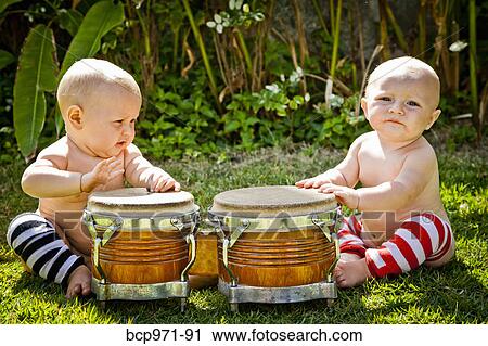 Stock Image - Twin babies playing drums outdoors. Fotosearch