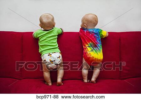 Two babies standing on red sofa View Large Photo Image Stock Photo - Two babies standing on red sofa. Fotosearch
