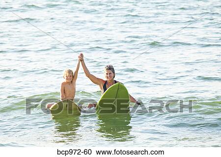 Stock Image - Woman and boy on surfboards in water. Fotosearch