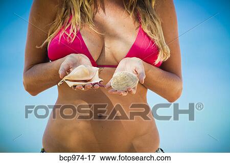 Stock Photo - Woman in bikini holding shells. Fotosearch