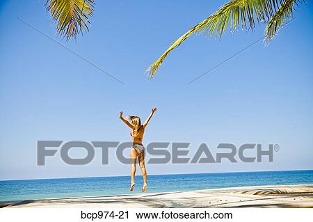 Stock Image - Woman in bikini jumping on beach. Fotosearch