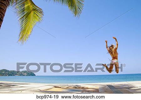 Stock Photo - Woman in bikini jumping on beach. Fotosearch