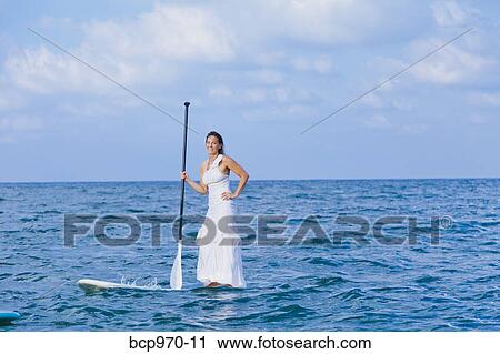 Woman in white dress riding paddle board View Large Photo Image Stock Image - Woman in white dress riding paddle board. Fotosearch