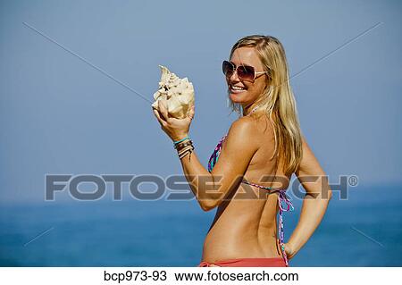 Woman on beach holding large seashell View Large Photo Image Stock Image - Woman on beach holding large seashell. Fotosearch