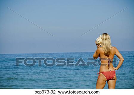Woman on beach listening to large seashell View Large Photo Image Stock Image - Woman on beach listening to large seashell. Fotosearch