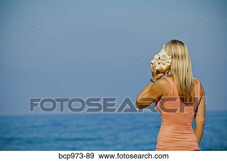 Woman on beach listening to large seashell View Large Photo Image Stock Photo - Woman on beach listening to large seashell. Fotosearch