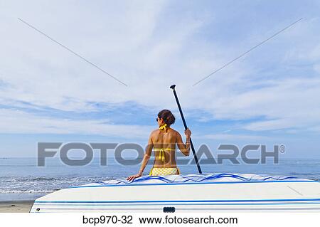 Stock Image - Woman on beach with paddle board. Fotosearch