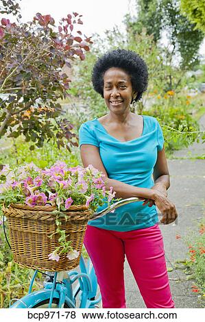 Stock Photo - Woman riding retro bicycle with flower basket. Fotosearch