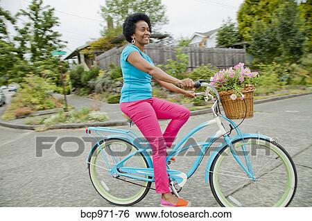 Stock Photograph - Woman riding retro bicycle with flower basket. Fotosearch