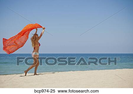 Stock Photography - Woman running on beach holding sarong. Fotosearch