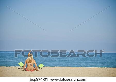 Stock Image - Woman wearing swim fins sitting on beach. Fotosearch