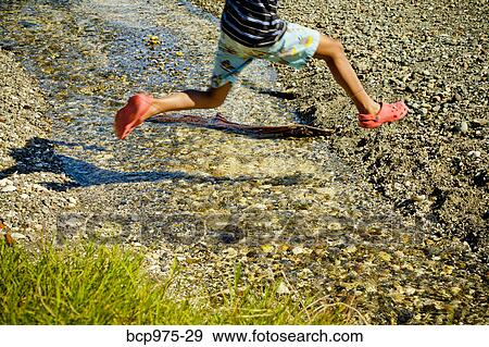 Stock Photo - Young boy jumping over creek on beach. Fotosearch