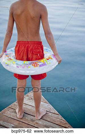 Stock Image - Young boy wearing float ring on dock. Fotosearch
