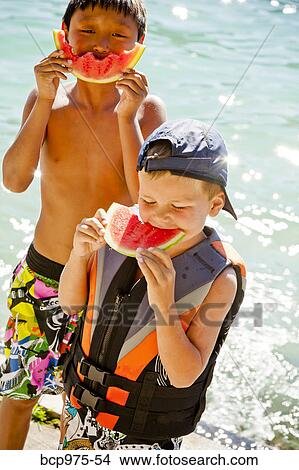 Picture - Young boys eating watermelon by lake. Fotosearch