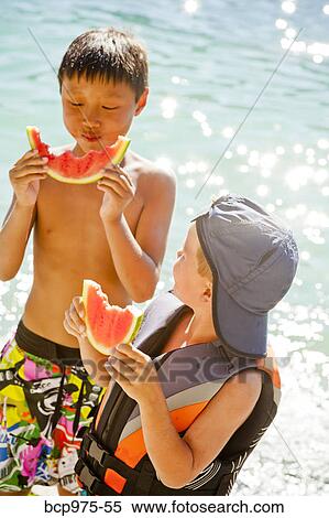 Stock Photography - Young boys eating watermelon by lake. Fotosearch