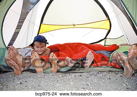 Picture - Young boy's face and pairs of feet poking out of tent. Fotosearch