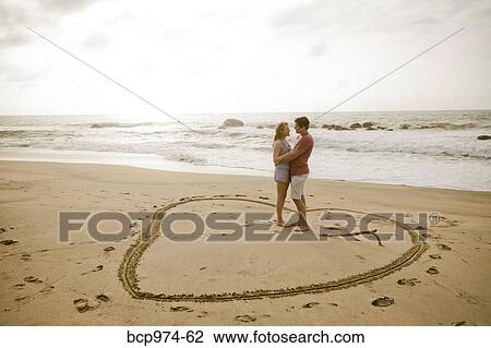 Young couple standing in heart design on beach View Large Photo Image Stock Image - Young couple standing in heart design on beach. Fotosearch